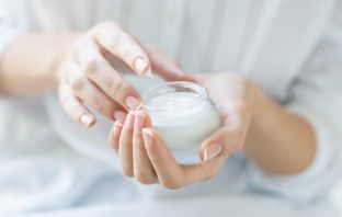 Closeup shot of hands applying moisturizer. Beauty woman holding a glass jar of night skin cream. Shallow depth of field with focus on moisturizer.