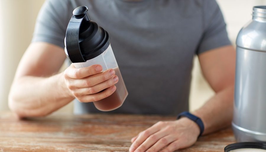 sport, healthy lifestyle and people concept - close up of man wearing fitness tracker with jar and bottle preparing protein shake